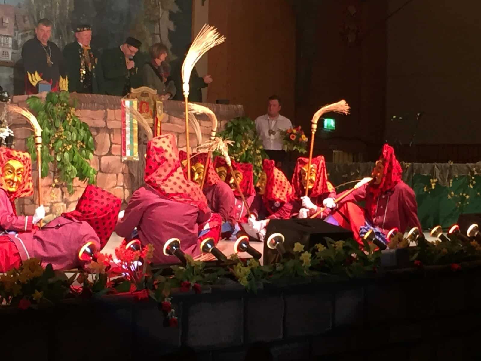 Tänzer des Hexenballetts der Hottscheck Narrenzunft sitzen auf der Bühne und halten ihre Besen