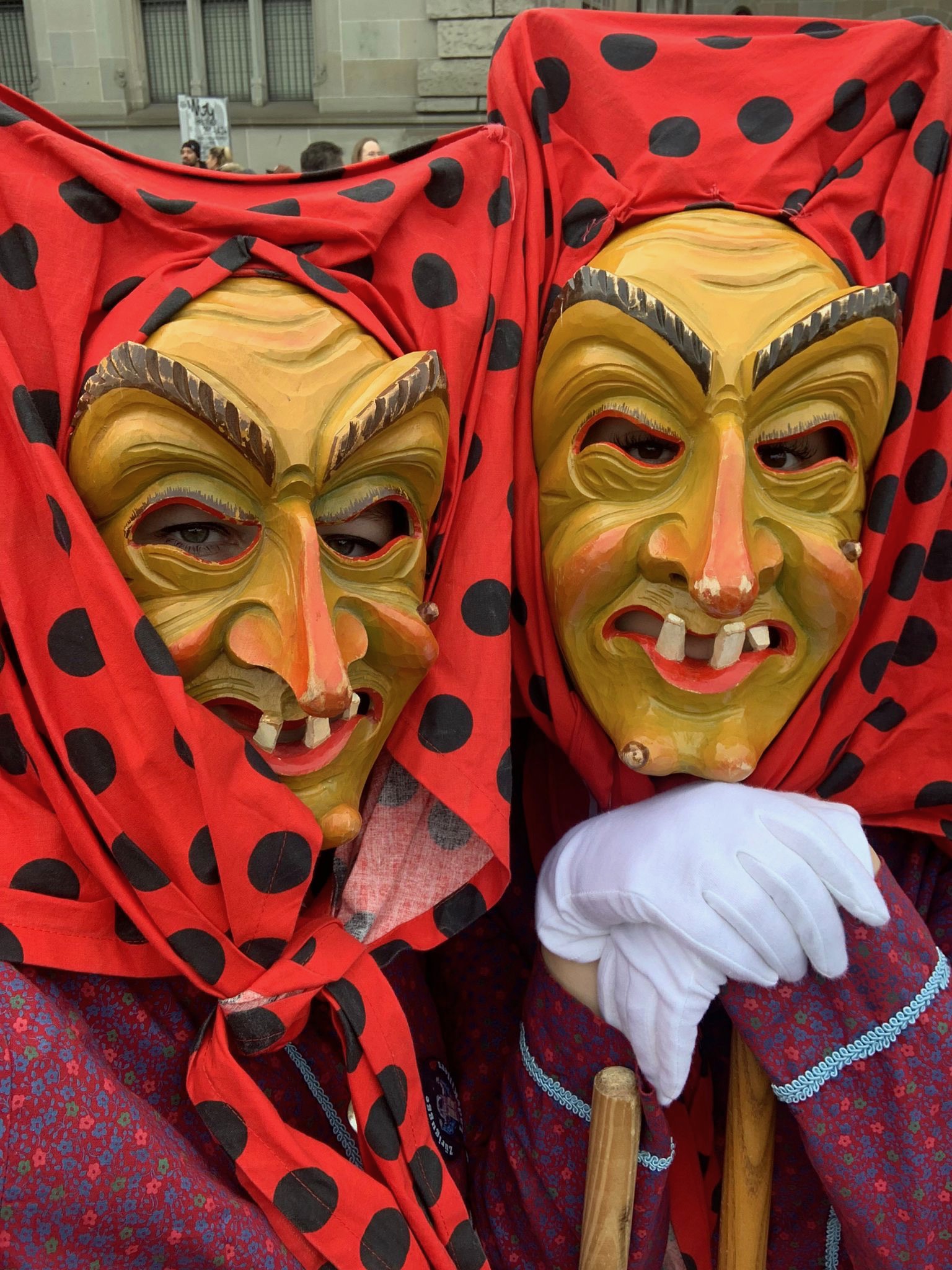 Zwei Hottscheck-Hexen in traditionellem Häs stützen sich auf ihre Besen und tragen Handschuhe